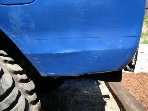 1979 Ford Bronco - Close-up of a blue vehicle's side panel, revealing a dent and a large off-road tire.