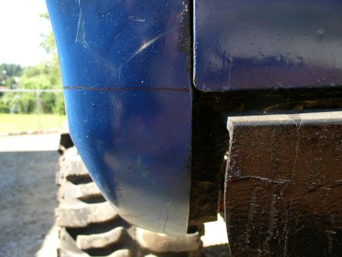 1979 Ford Bronco - Close-up view of a blue vehicle's body panel and a large tire, with 'SUPERMOTORS' text visible at the bottom.