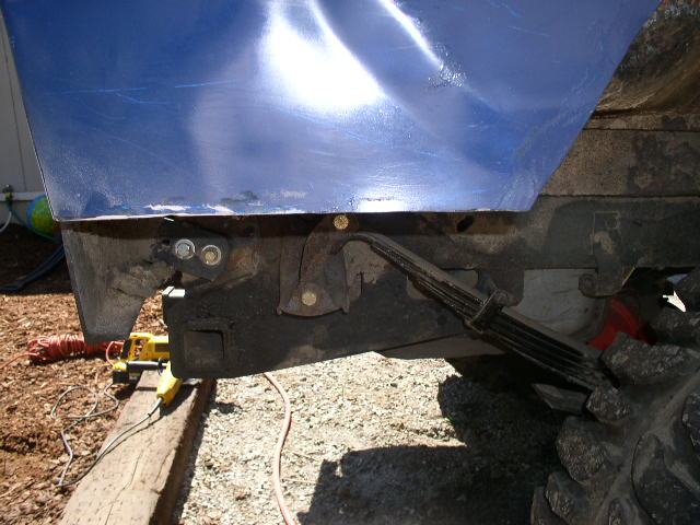 Close-up of a vehicle's rear leaf spring and frame, with a blue body panel above