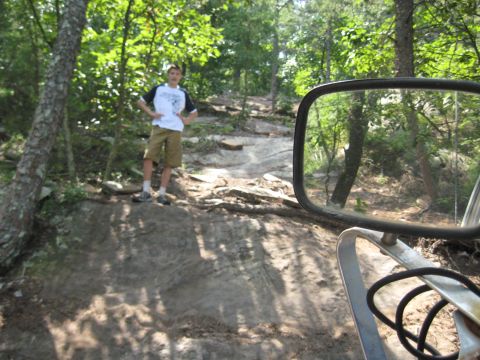 1978 Ford Bronco - A boy stands on a rocky trail in a wooded area, seen through a vehicle's side mirror.