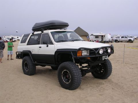 1985 Toyota 4Runner - A modified 1985 Toyota 4Runner with a cargo box and large tires sits on a sandy beach with campers in the background.