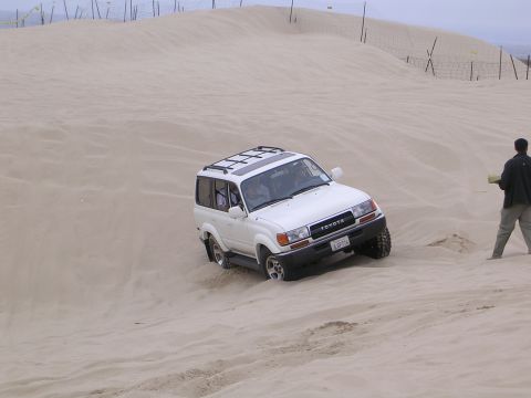 1985 Toyota 4Runner - White Toyota Land Cruiser navigating sand dunes with a person standing nearby.