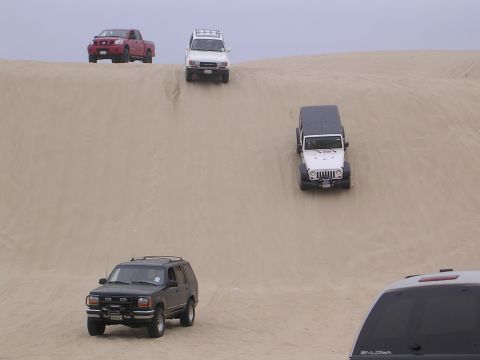 1985 Toyota 4Runner - Multiple vehicles navigate sandy terrain, with a red truck and white SUV at the top of a dune.