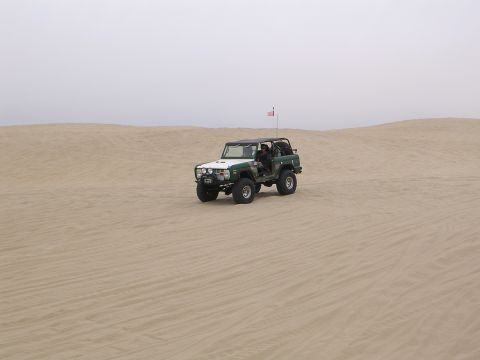 1985 Toyota 4Runner - A two-tone off-road vehicle navigates sandy terrain with an American flag flying from its antenna.