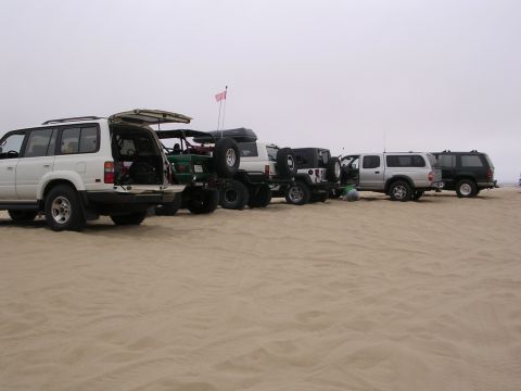 1985 Toyota 4Runner - A line of SUVs and trucks are parked on a sandy beach, with the rear hatch of the first vehicle open.