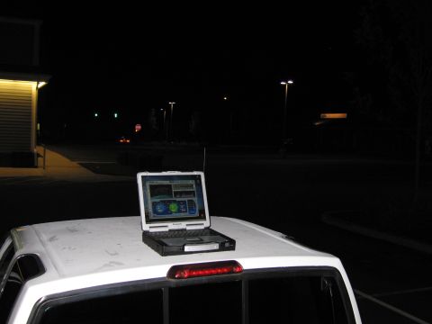 2001 Ford Crown Victoria - A laptop is placed on the roof of a white pickup truck at night, displaying GPS information on its screen.