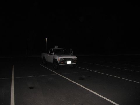 2001 Ford Crown Victoria - A white pickup truck sits alone in a dimly lit parking lot under the night sky.