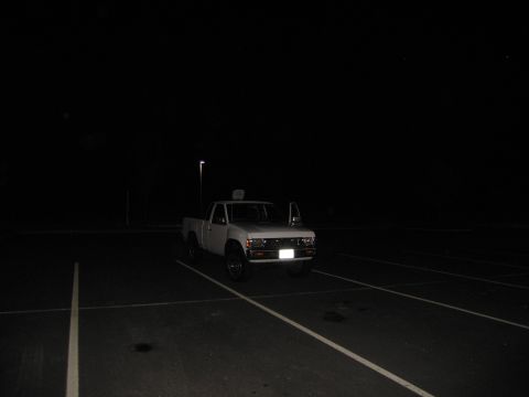 2001 Ford Crown Victoria - A white pickup truck is parked in a dimly lit parking lot at night, with its doors open.