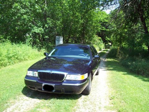 1999 Mercury Grand Marquis - Sedan parked on a dirt road surrounded by trees and grass. The grille and headlights are visible.