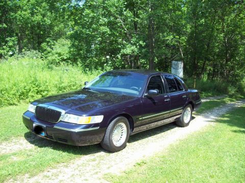1999 Mercury Grand Marquis - A 1999 Mercury Grand Marquis sedan is parked on a gravel path surrounded by greenery.