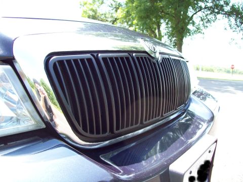 1999 Mercury Grand Marquis - Close-up of a Mercury sedan's chrome vertical-bar waterfall grille and hood-crest emblem on a dark blue car.