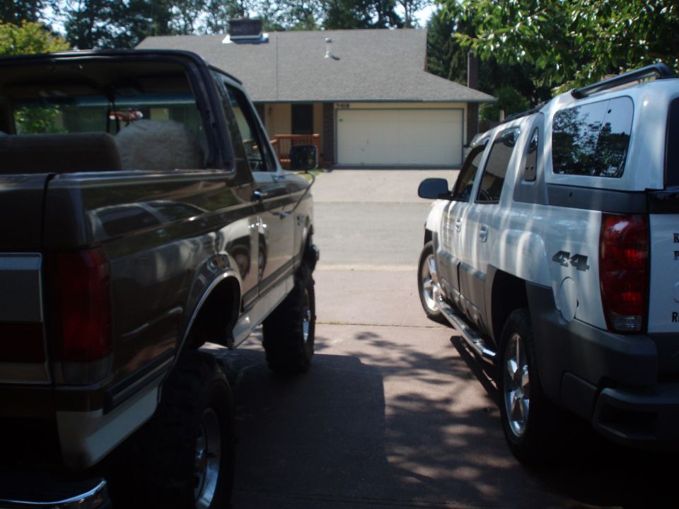 Dark brown Ford Bronco with lifted suspension and chrome wheels parked next to a white Chevrolet Avalanche
