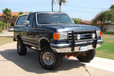 1991 Ford Bronco - This 1991 Ford Bronco features a dark blue exterior with a tan removable top and prominent aftermarket accessories.