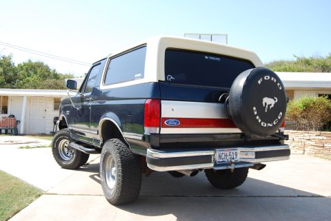1991 Ford Bronco - This 1991 Ford Bronco is shown from the rear, a dark blue body with a tan removable top and a spare tire mounted on the tailgate.
