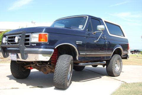 1991 Ford Bronco - This lifted Ford Bronco sits on a paved driveway under a clear blue sky.