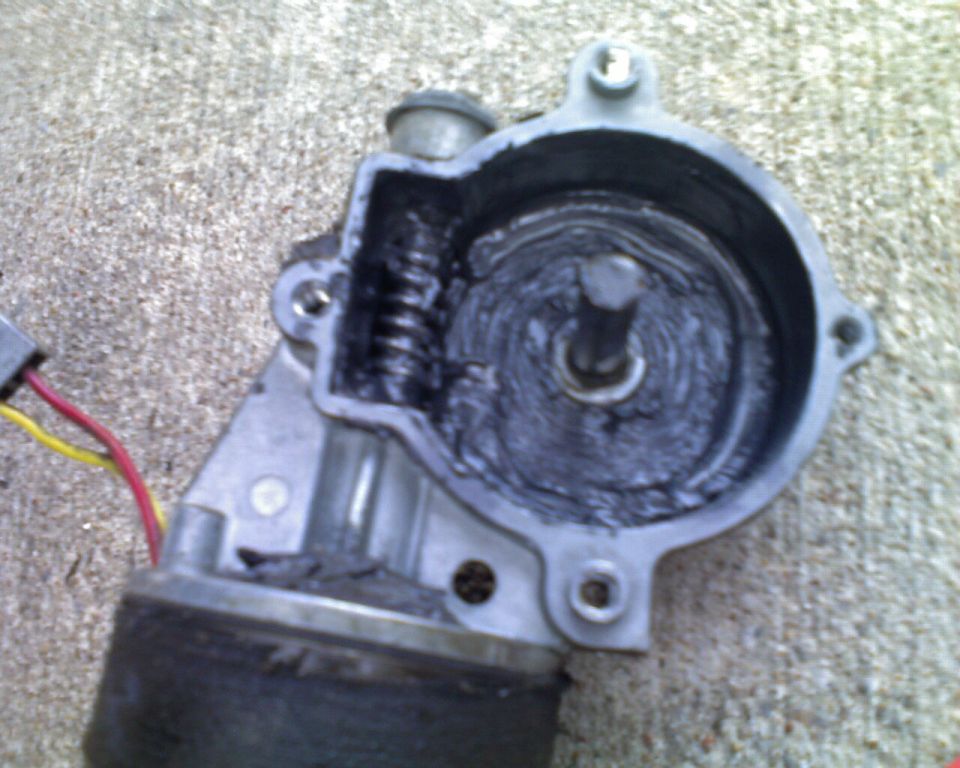 Opened electric gear motor showing worm gear and grease-covered drive gear, red and yellow wires, on concrete
