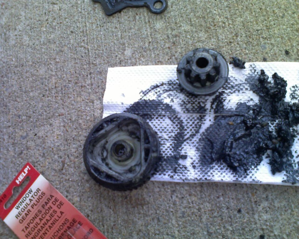 Window regulator gear parts and black grease on a paper towel, next to a HELP! brand package for window regulator gear plugs