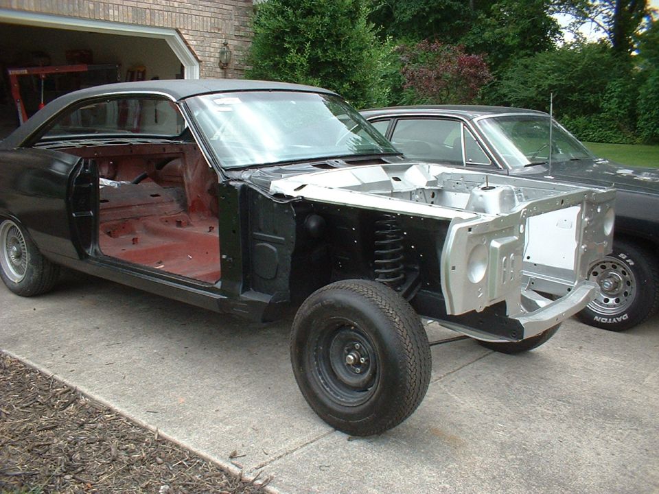 Black 1960s hardtop coupe under restoration, front sheet metal off and engine bay in silver primer