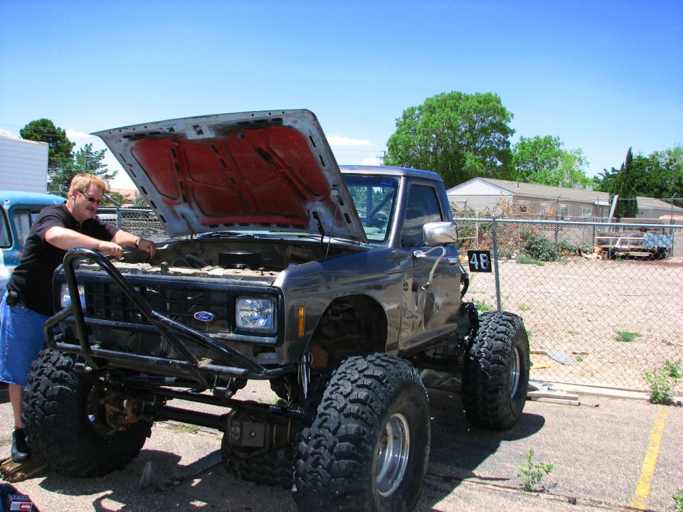 Man working on lifted Ford Bronco II with hood open, large off-road tires