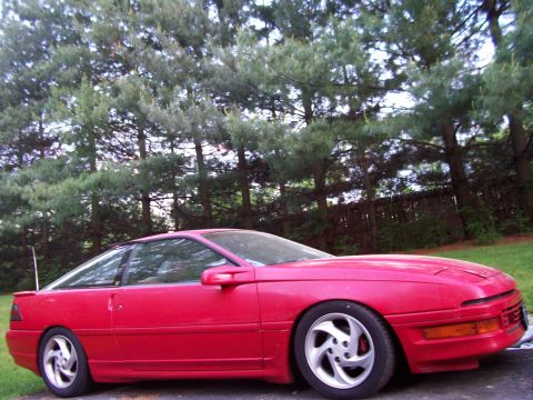 1989 Ford Probe - A red coupe is parked in front of a line of trees.
