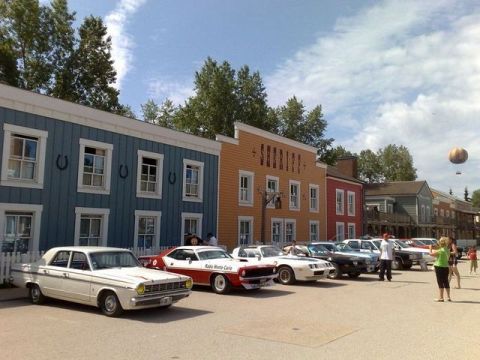 1991 Ford LTD Crown Victoria - A line of vintage cars are parked outside buildings designed in a western theme. A hot air balloon floats overhead.