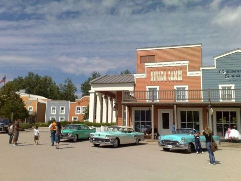 1991 Ford LTD Crown Victoria - A collection of vintage automobiles are displayed in front of a western-themed town facade under a partly cloudy sky.