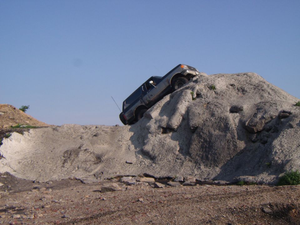 Dark SUV climbing a large dirt mound, angled to the right