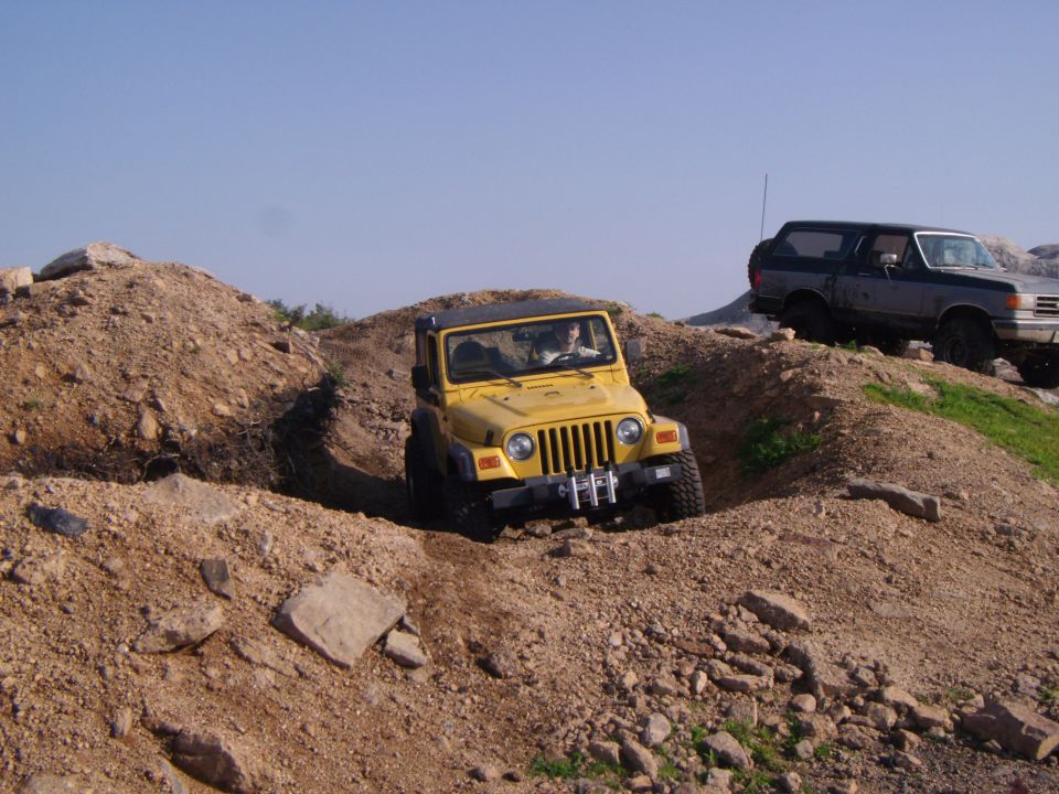 Yellow 2003 Jeep Wrangler driving on dirt hill, another truck behind