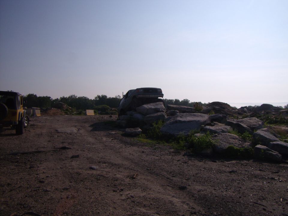 Yellow Jeep Wrangler parked on dirt road, another Jeep Wrangler stuck on large rocks