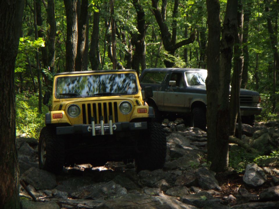 Yellow Jeep Wrangler with winch on rocky trail, blue and grey Ford Bronco behind it