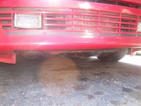 1989 Ford Probe - Close-up view of a red car's front bumper and grille, showing a headlight and the horizontal grille pattern.