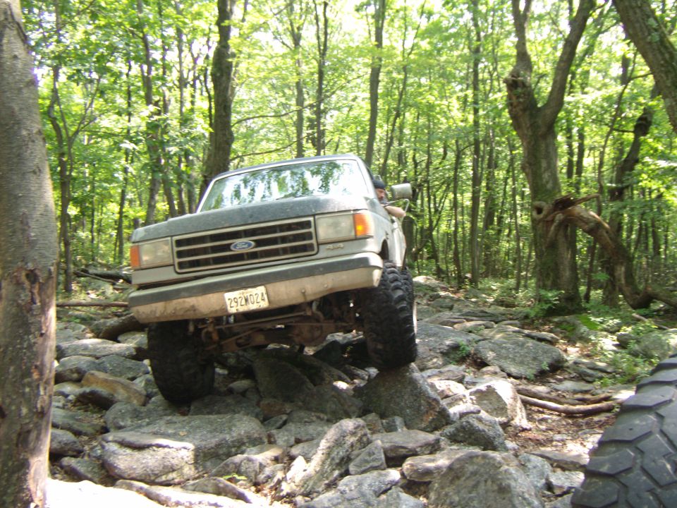 Ford Bronco navigating a rocky trail in a forest. License plate reads 292W024