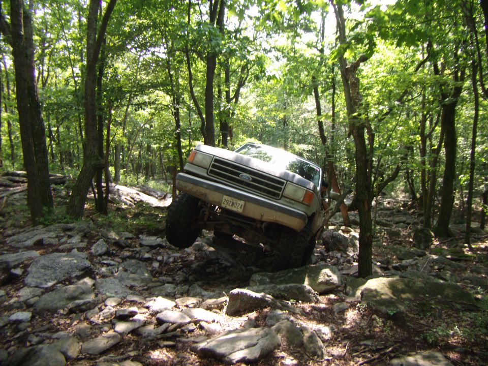Silver Ford F-Series truck navigating a rocky, wooded trail