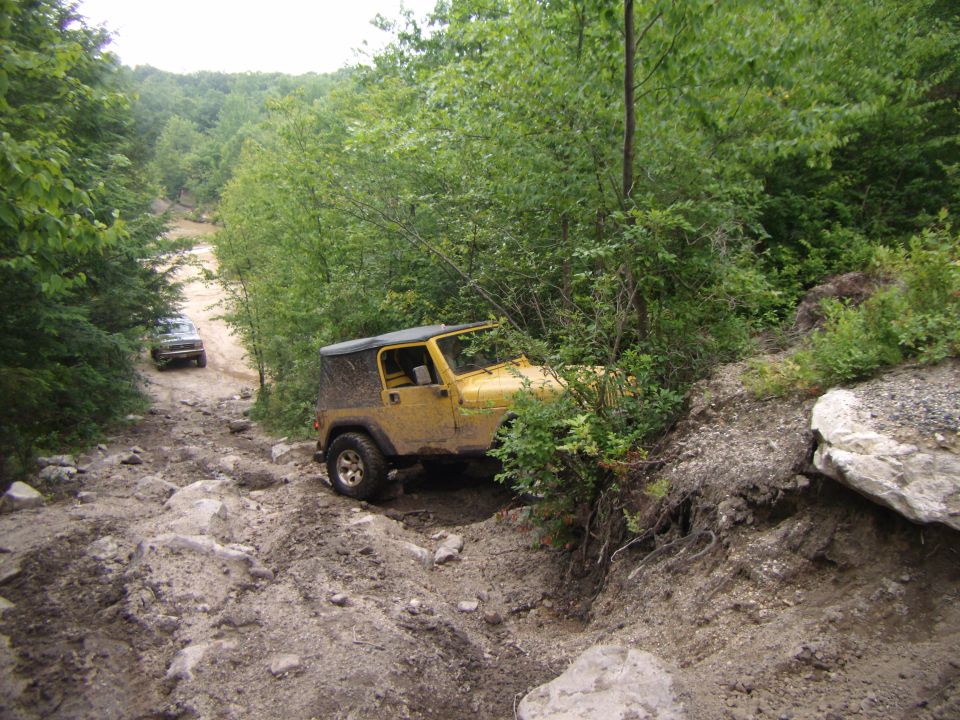 Yellow Jeep Wrangler on a rocky, off-road trail, partially obscured by bushes