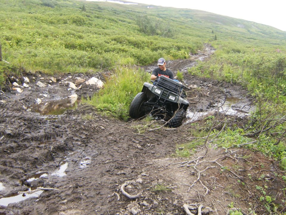 Green all-terrain vehicle navigating a muddy trail with a person riding it