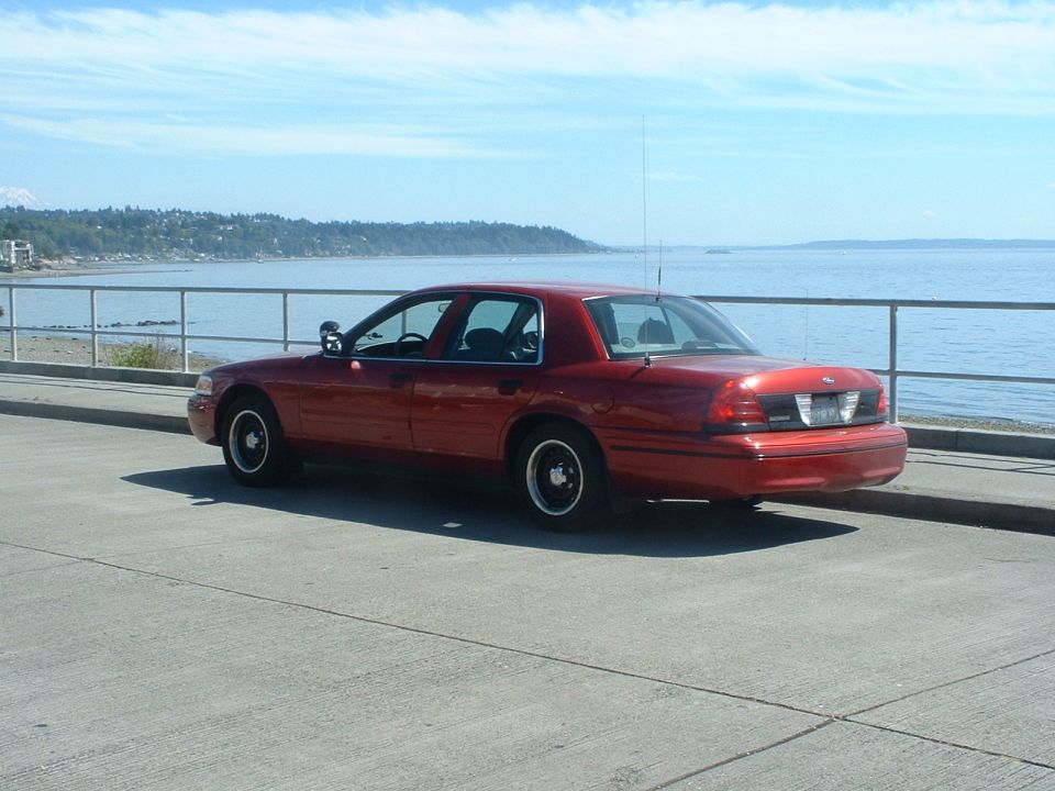 Red Ford Crown Victoria with black steel wheels and whip antenna parked at a waterfront overlook