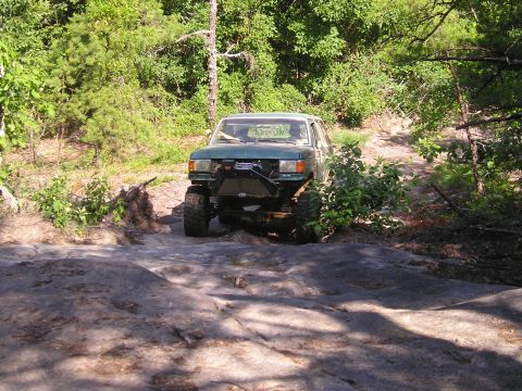 1989 Ford Bronco - A modified green SUV navigates a rocky trail surrounded by dense foliage.