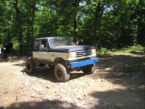 1989 Ford Bronco - This lifted 1987 Ford Bronco navigates a dirt path in a wooded area, a prominent blue aftermarket bumper.