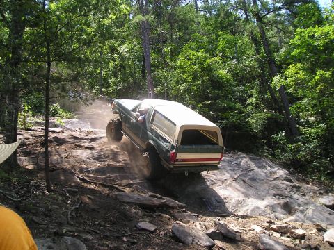 1989 Ford Bronco - A 1989 Ford Bronco navigates a challenging rocky trail in a wooded area.