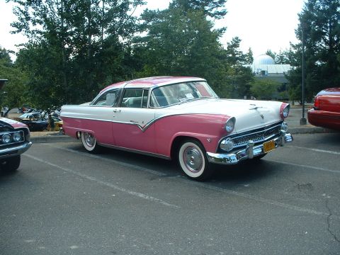 1999 Ford Crown Victoria - A classic two-tone pink and white Ford Fairlane is parked in a lot, with other vehicles visible in the background.