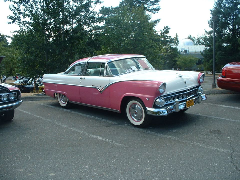 Two-tone pink and white 1955 Ford Fairlane parked next to another car