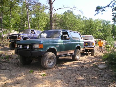 1989 Ford Bronco - Three Ford Broncos are parked on a dirt trail in a wooded area.