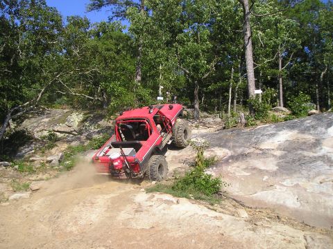 1989 Ford Bronco - This modified SUV navigates a challenging off-road trail with steep rocks and loose dirt.