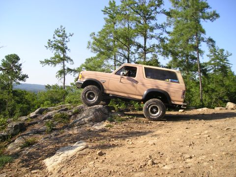 1989 Ford Bronco - A tan Ford Bronco navigates a challenging rocky terrain on a sunny day.