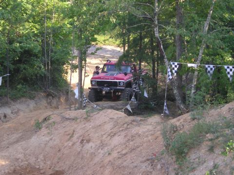 1989 Ford Bronco - Off-road vehicle navigates a challenging dirt track course with checkered flags marking the way.