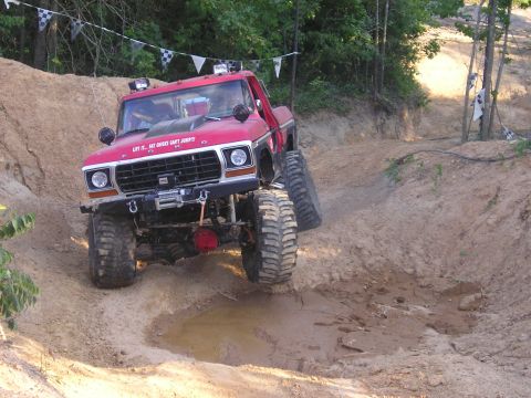 1989 Ford Bronco - This modified pickup truck navigates a challenging off-road course with checkered flags visible in the background.