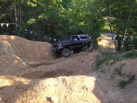 1989 Ford Bronco - A black Ford Bronco navigates a challenging off-road course with checkered flags adorning the trees.