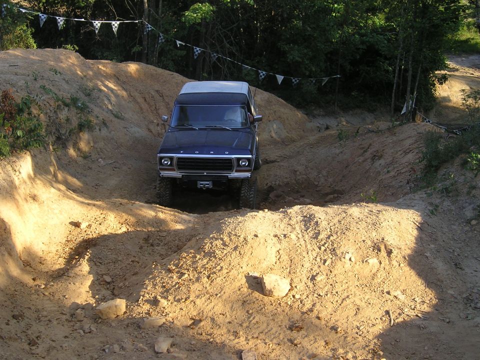Blue Ford Bronco driving on a dirt track, front view