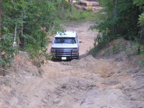 1989 Ford Bronco - White van navigates a challenging dirt path through a wooded area.