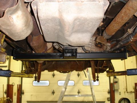1979 Ford Bronco - A black crossmember is installed beneath the transmission and exhaust system of a vehicle.